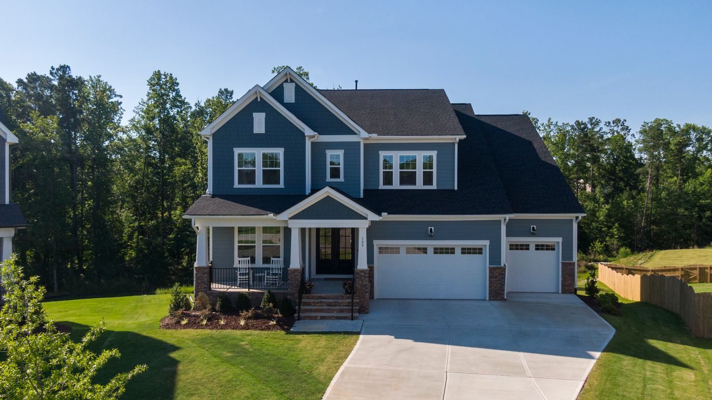 Blue-gray two-story home with a front porch, rocking chairs, and a wide driveway on a tree-lined street